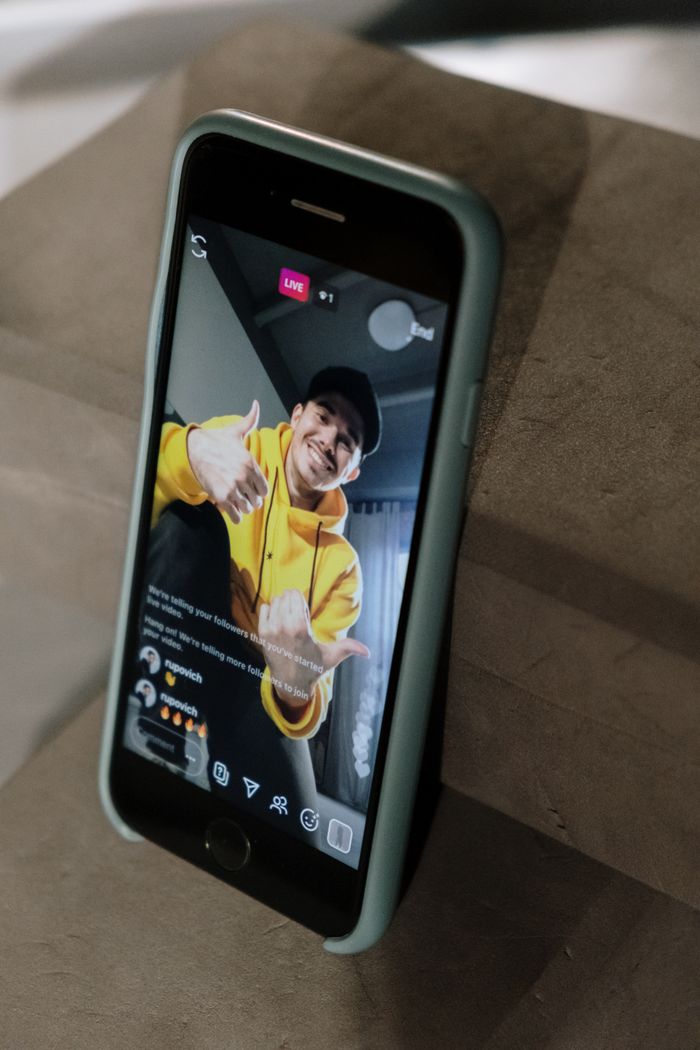 Un homme portant un sweat à capuche jaune participe à une diffusion en direct sur l’écran d’un smartphone, à l’intérieur.